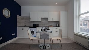A modern kitchen with white cabinets, a washing machine, and a dining area with two chairs and a table. - Cross St Boutique Apartment (Altrincham)