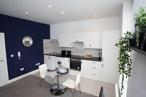 A modern kitchen with white cabinets, a black countertop, and a built-in oven. There is a dining area with a table and chairs.