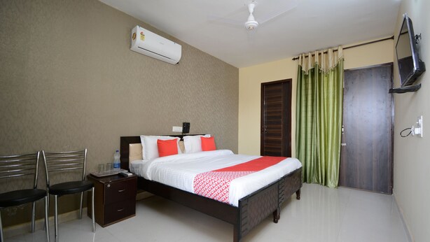 A neatly arranged bedroom with a bed, bedside table, chair, and an air conditioning unit. - OYO 37658 King Palace (Mohali)