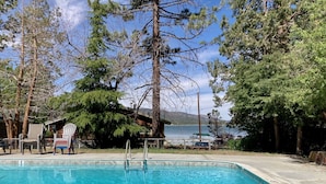 Una piscina rectangular con agua azul cristalina, rodeada de árboles y una cabaña de madera al fondo.