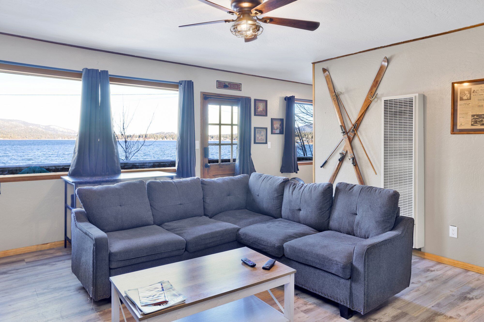 A modern living room with a gray sectional sofa, a wooden coffee table, and a view of a lake through large windows.