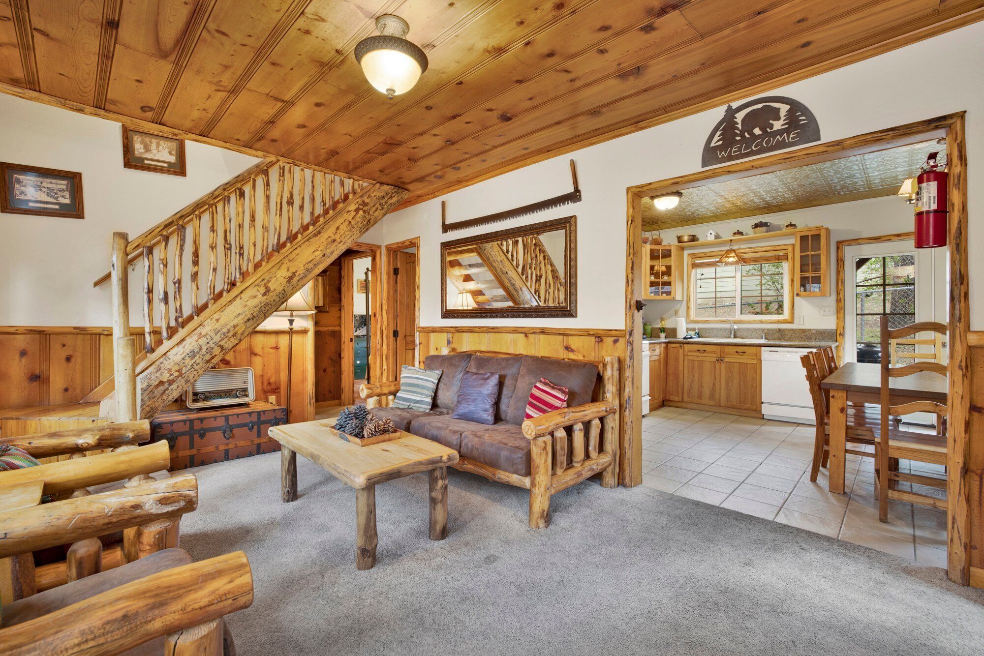 A rustic interior with a wooden staircase, a sofa, a dining table, and a kitchen area.