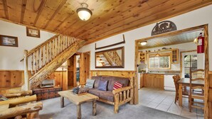 A rustic interior with a wooden staircase, a sofa, a dining table, and a kitchen area. - Nine Pines Lodge#537 (Big Bear City)