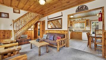 A rustic interior with a wooden staircase, a sofa, a dining table, and a kitchen area.