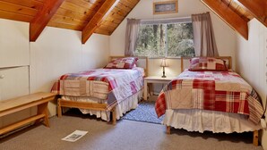 Um quarto de sótão aconchegante com duas camas de madeira, uma escrivaninha pequena e uma janela com cortinas.