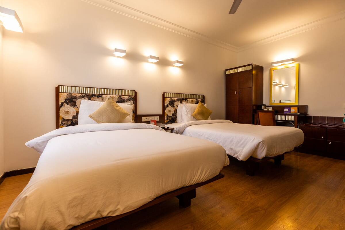 A hotel room with two beds, wooden flooring, a wardrobe, and a mirror with a gold frame.