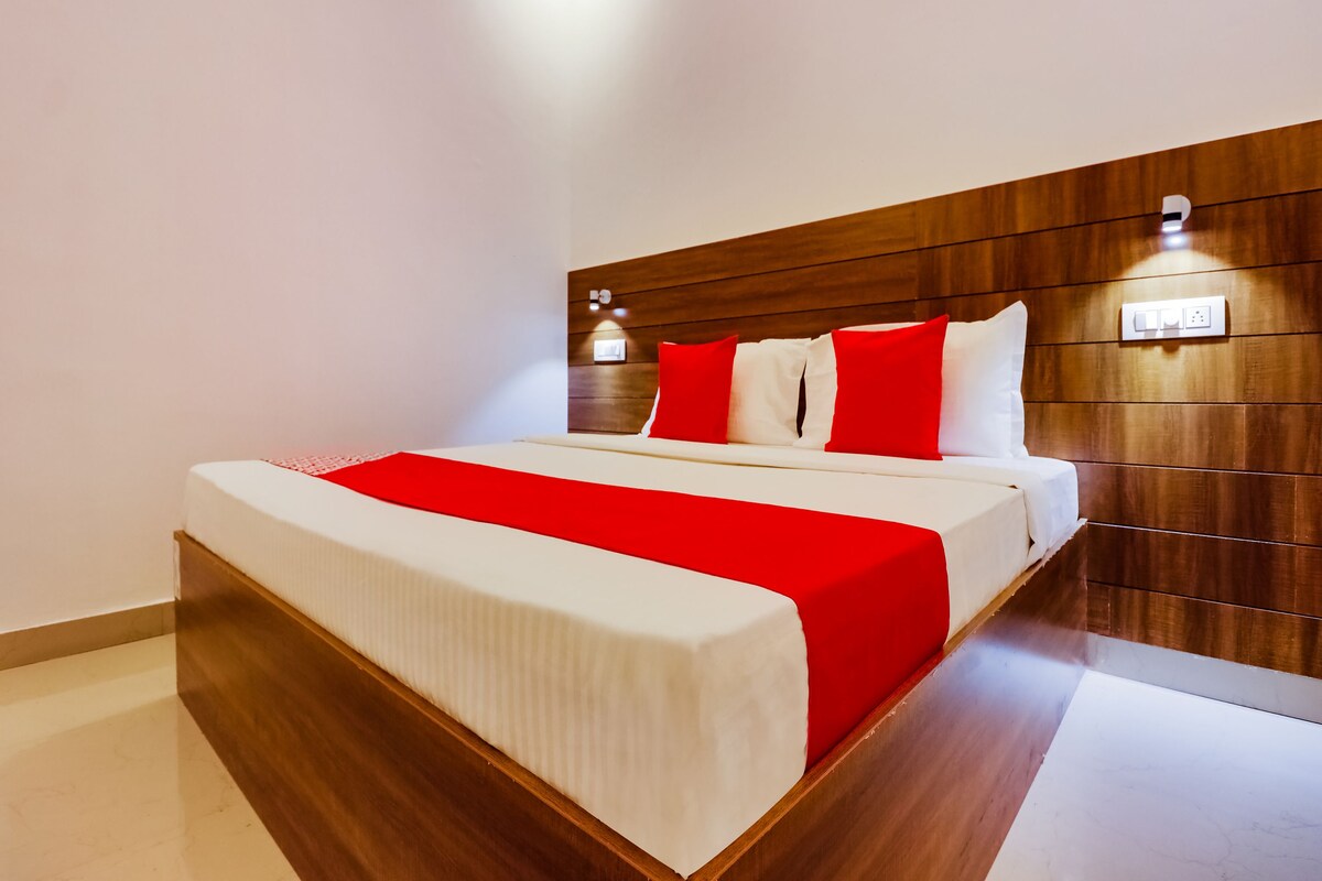 A modern hotel room with a wooden headboard, a large bed with white and red bedding, and a small bedside table.