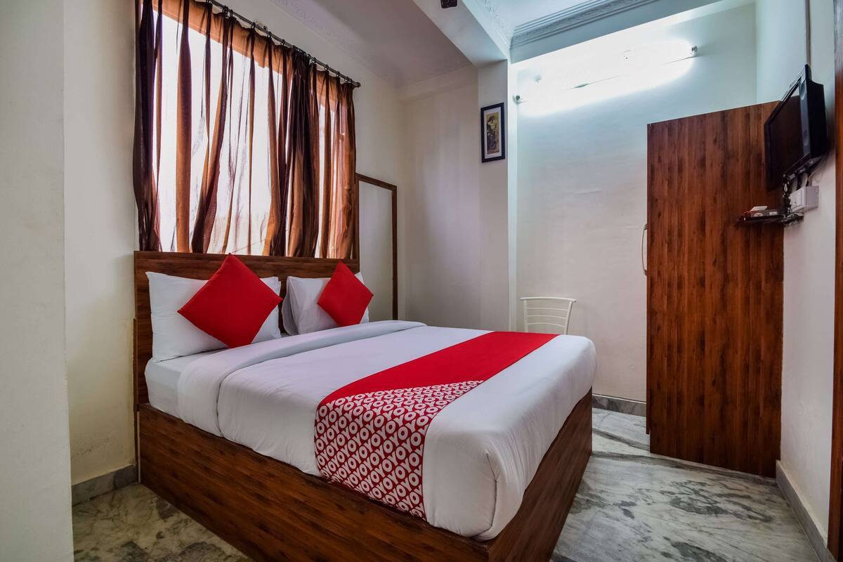 A neatly made bed with a wooden headboard, red and white bedding, and a red throw blanket.