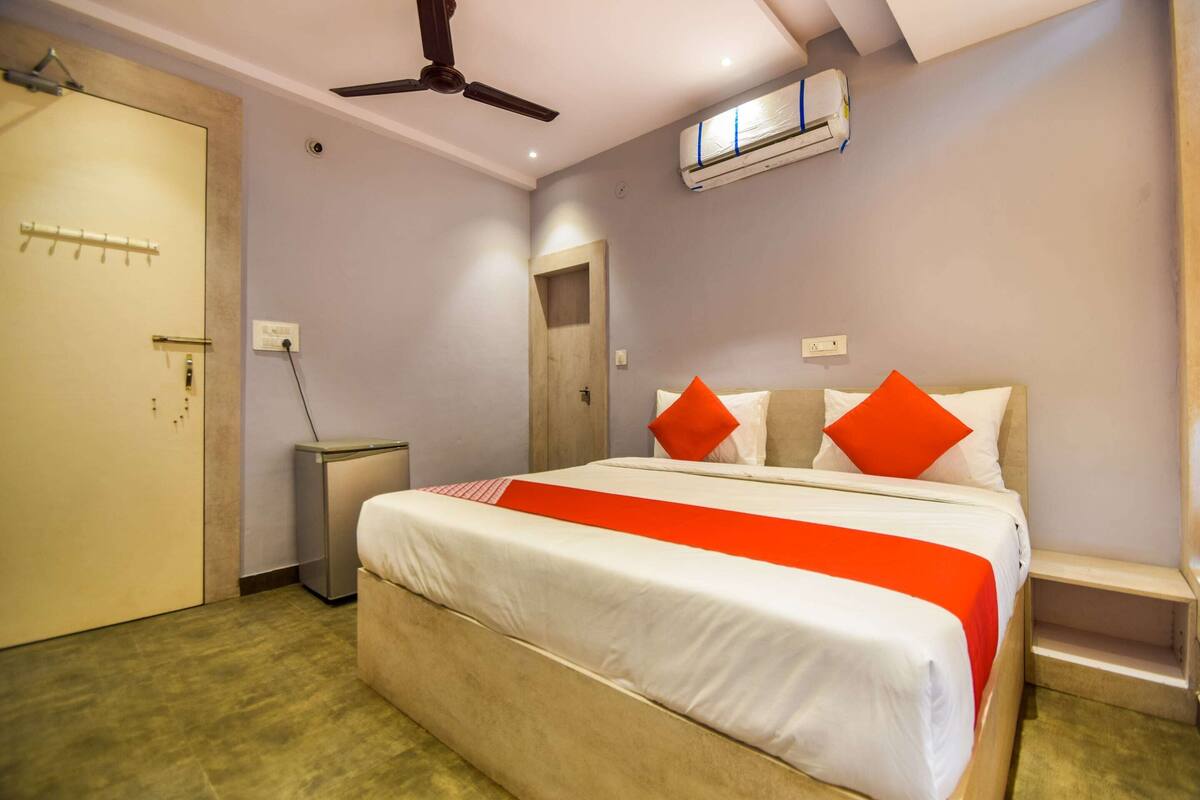 A hotel room with a bed, a ceiling fan, an air conditioning unit, a bedside table, and a wardrobe.