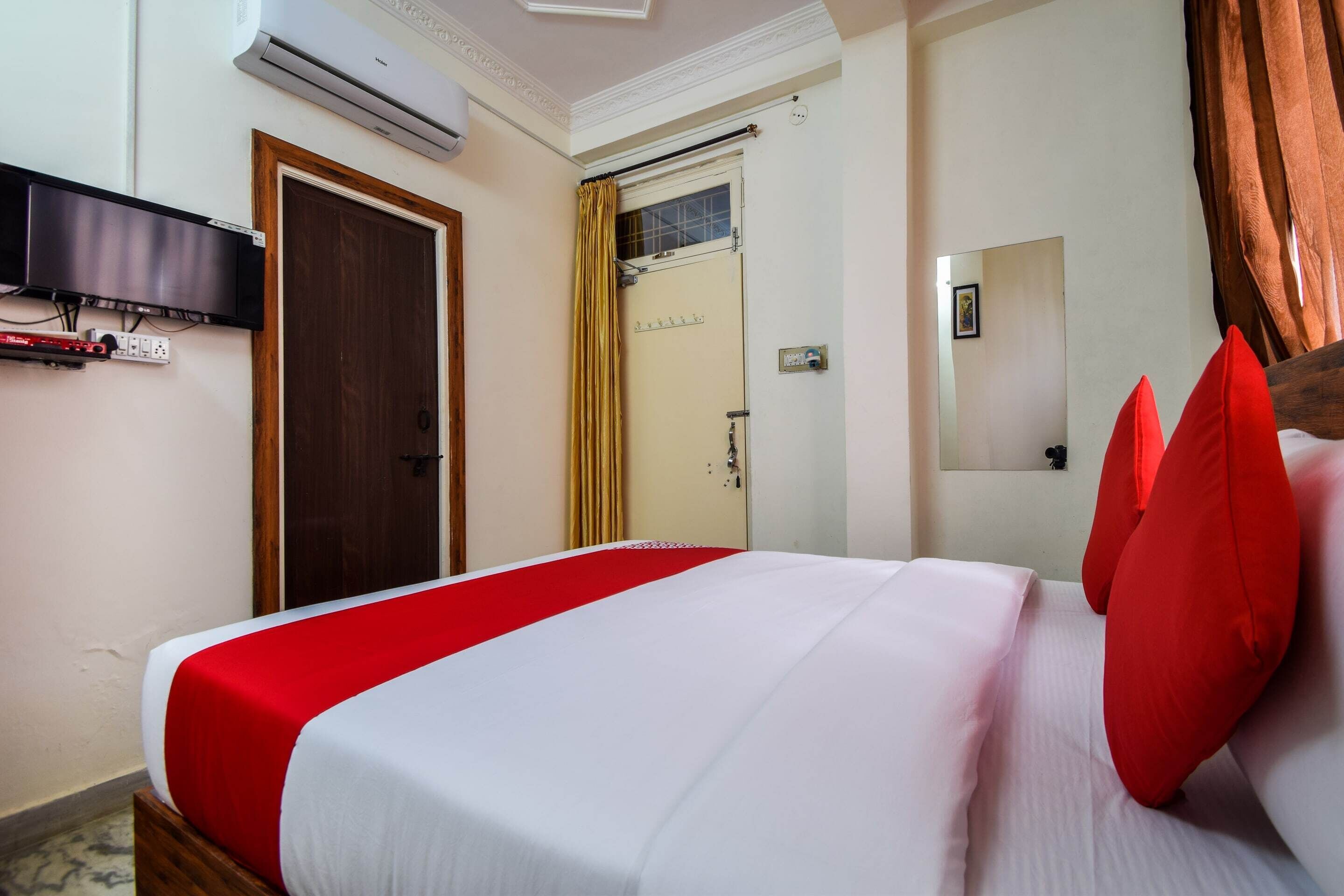 A hotel room with a bed, a TV mounted on the wall, and a door with a curtain.