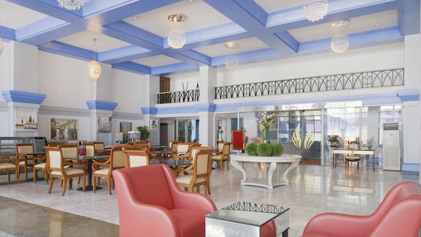 A spacious lobby with high ceilings, chandeliers, and a mix of seating areas including red chairs and wooden tables. - Capital O 44162 Royal Palms Hotel - Rose Collection (Mumbai)