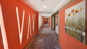 A hallway with red walls, a patterned carpet, and a painting of flowers. - Capital O 44162 Royal Palms Hotel - Rose Collection (Mumbai)
