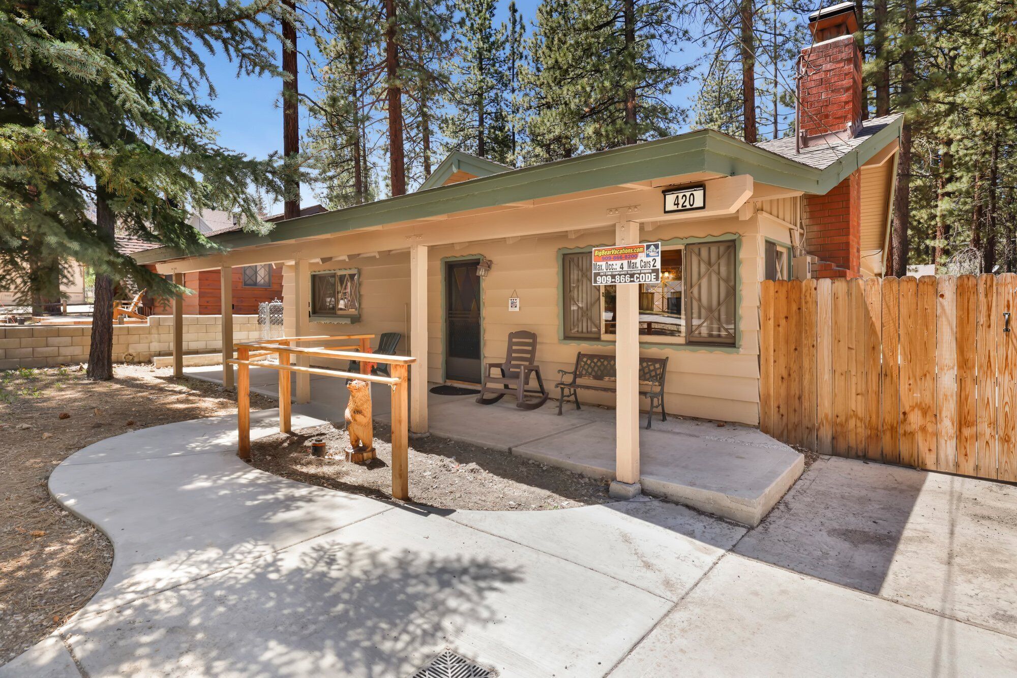 A small, single-story cabin with a green roof, a wooden deck, and a fenced yard.