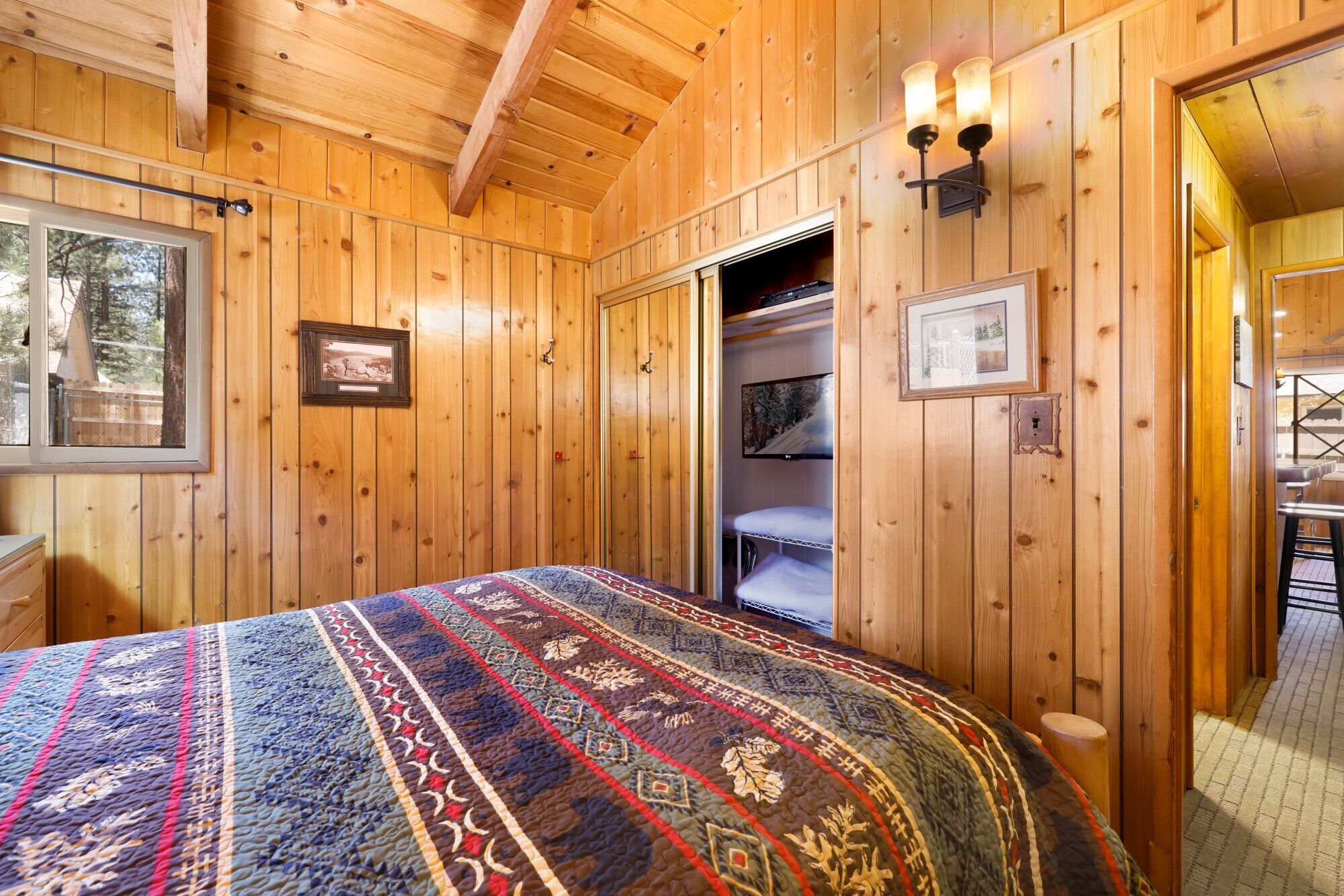 Ein Zimmer in einer Holzhütte mit einem Bett, einem Fenster, einer Tür und einem Wand-Fernseher.