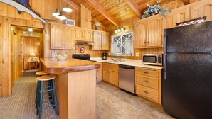 A wooden cabin kitchen with a black refrigerator, wooden cabinets, a sink, a microwave, and a stove. - Oriole Cottage #621 (Big Bear Lake)