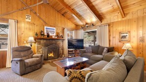 A cozy log cabin interior with a stone fireplace, wooden walls, a comfortable sofa, and a television. - Oriole Cottage #621 (Big Bear Lake)