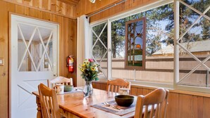 A wooden interior with a dining table, chairs, a vase with flowers, and a window with a view of trees. - Oriole Cottage #621 (Big Bear Lake)