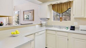 A kitchen with white cabinets, a coffee maker, a sink, and a window with a brown valance. - Bear Mountain Chalet #639 (Big Bear Lake)