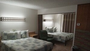 Une chambre d’hôtel avec deux lits, une chaise, une petite table et un luminaire fixé au mur.