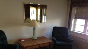 Un salon avec une table en bois, une lampe, une chaise et un miroir au mur.