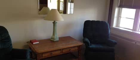 A living room with a wooden table, a lamp, a chair, and a mirror on the wall.