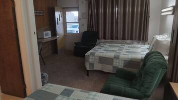 Habitación de hotel con cama, una silla, escritorio con microondas y ventana con cortinas.