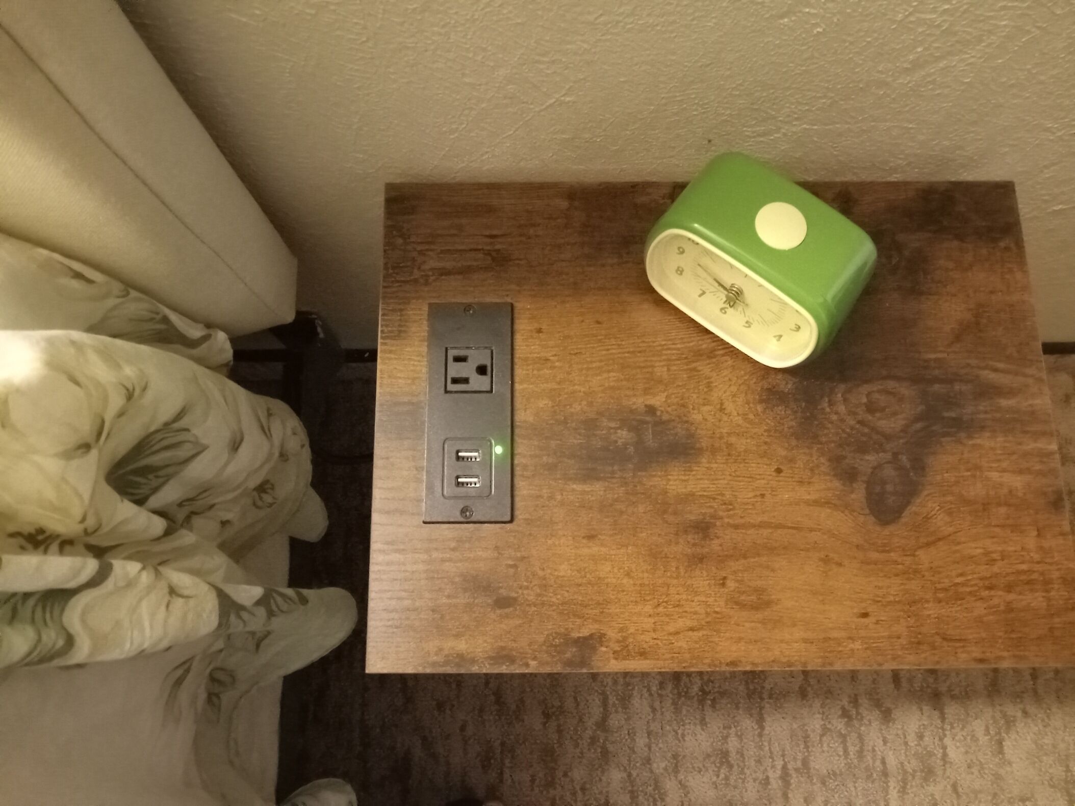 Ein Holztisch mit einer grünen Uhr und einer Steckdose.