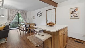 Una cocina moderna con una isla de madera, un comedor con sillas, un sofá y un amplio ventanal con cortinas.