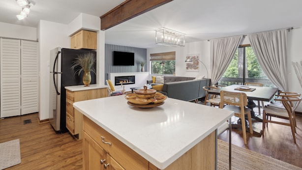 Una cocina moderna con armarios de madera, un refrigerador negro y un comedor con mesa y sillas.