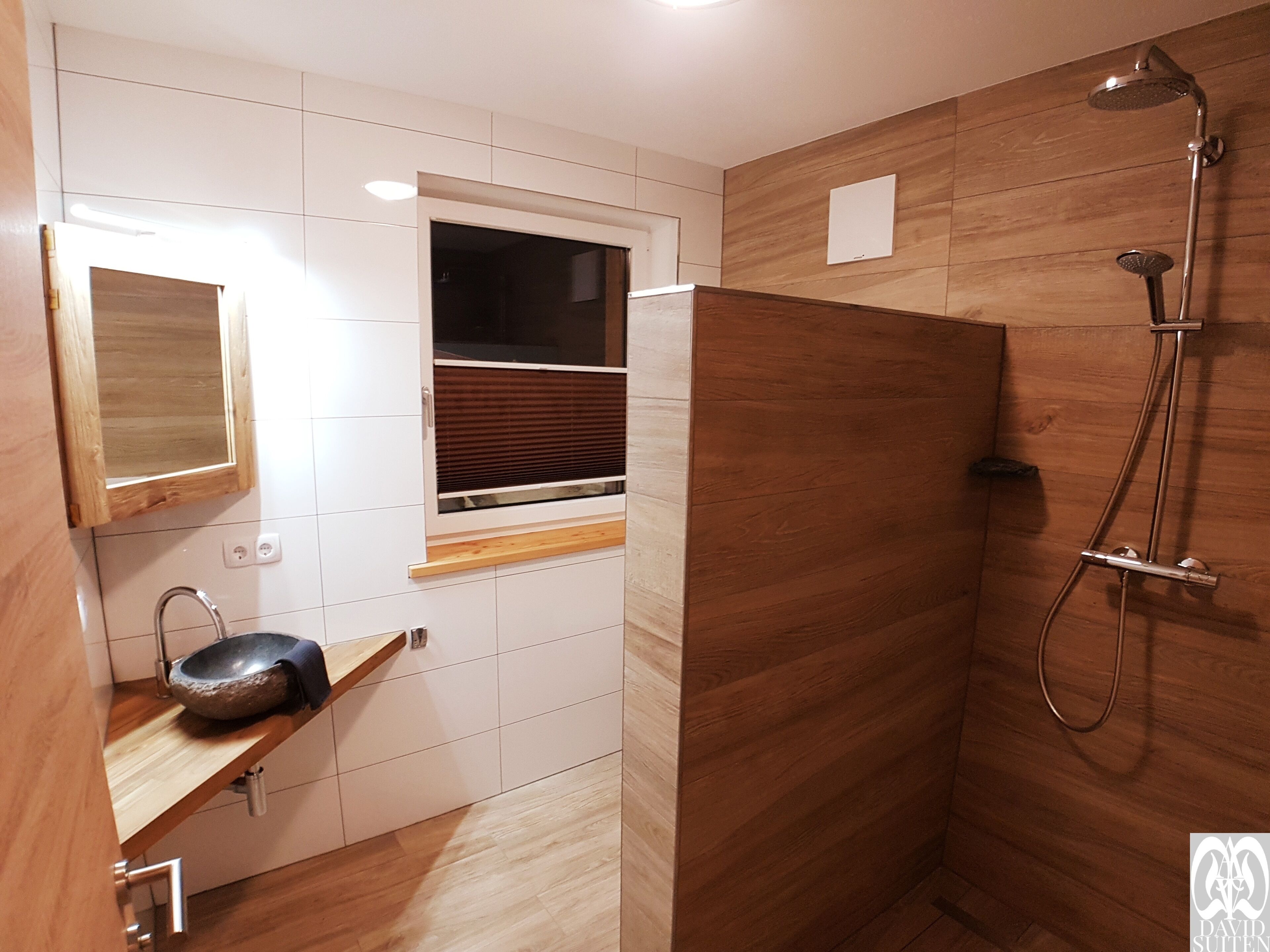 A bathroom with a wooden shower enclosure, a sink with a stone basin, and a window with blinds.