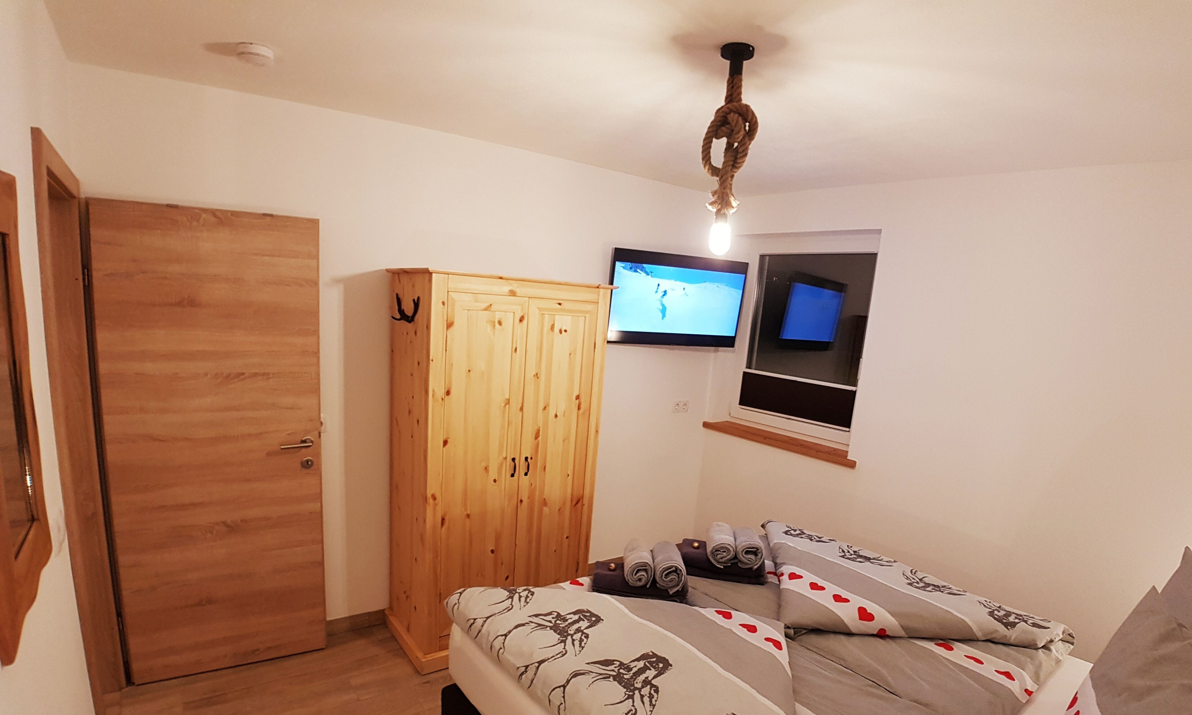 Un dormitorio con un armario de madera, una cama con ropa de cama estampada y un televisor montado en la pared.