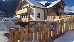 A chalet-style hotel with wooden balconies and a snow-covered roof, surrounded by a wooden fence and snow. - David Suiten (Mauterndorf)