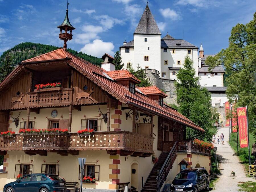 Un edificio de madera tradicional con un balcón, una escalera y una vista de un castillo al fondo.