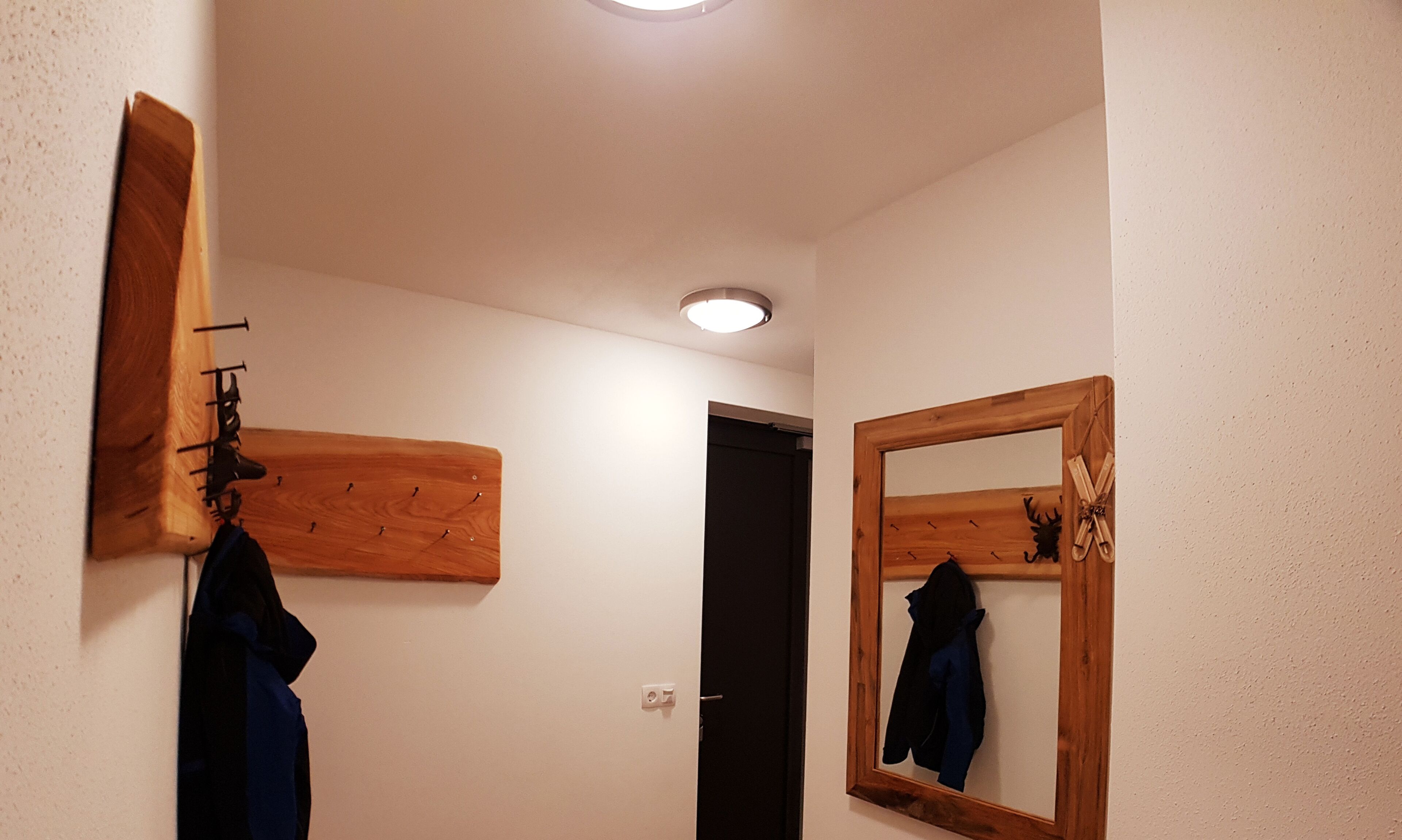 Un corridoio stretto con un appendiabiti in legno, uno specchio e una porta.