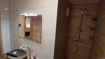 A bathroom with a wooden vanity, a stone sink, a mirror, and a shower with a wooden wall.