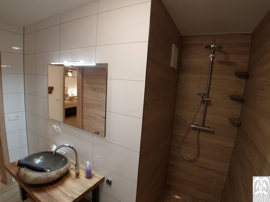 A bathroom with a wooden vanity, a stone sink, a mirror, and a shower with a wooden wall.