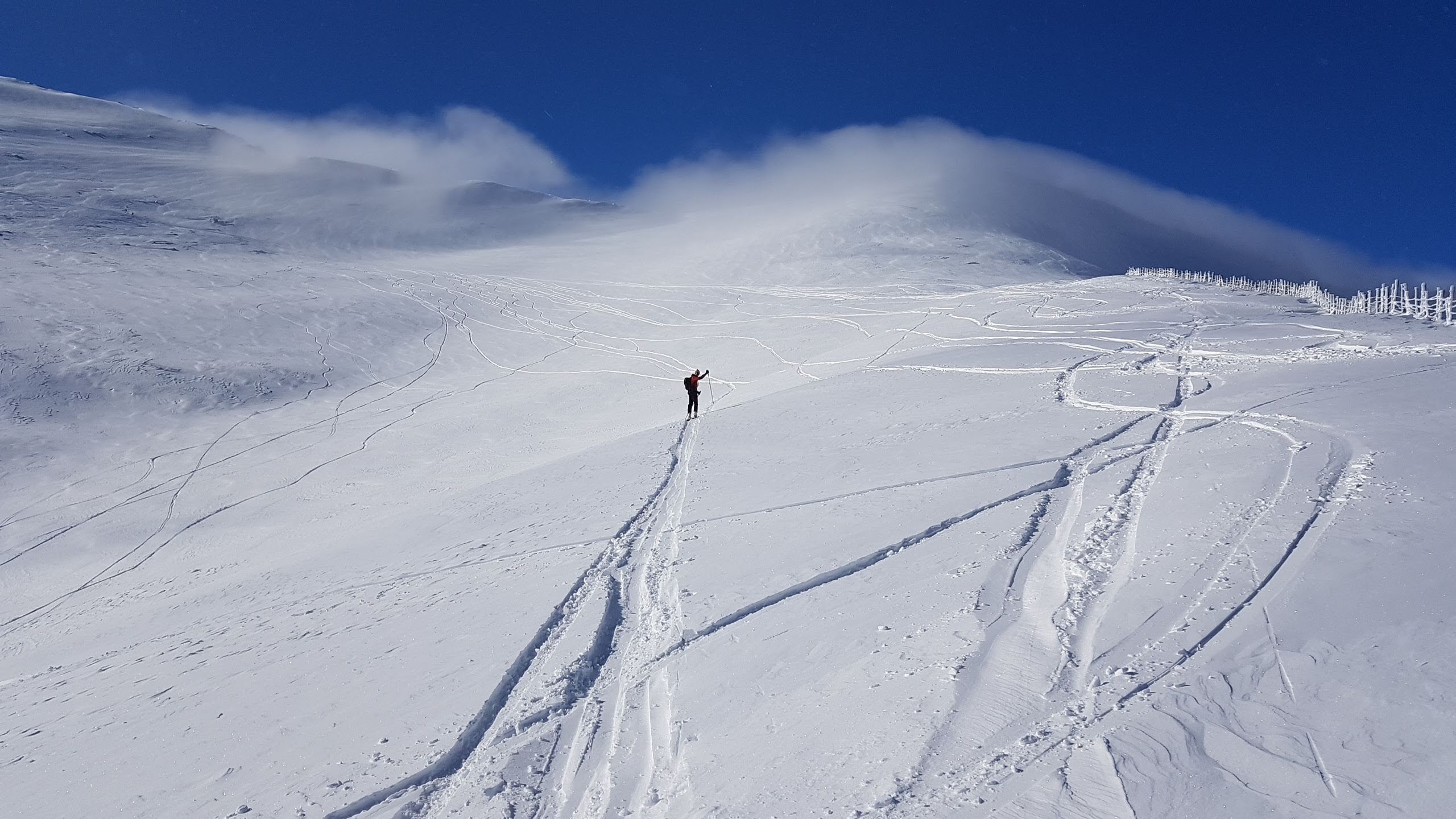 Paisaje montañoso nevado con un solo esquiador a lo lejos.