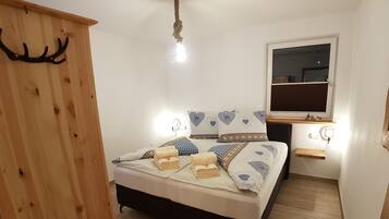 A bedroom with a bed, wooden wardrobe, bedside table, and a window.