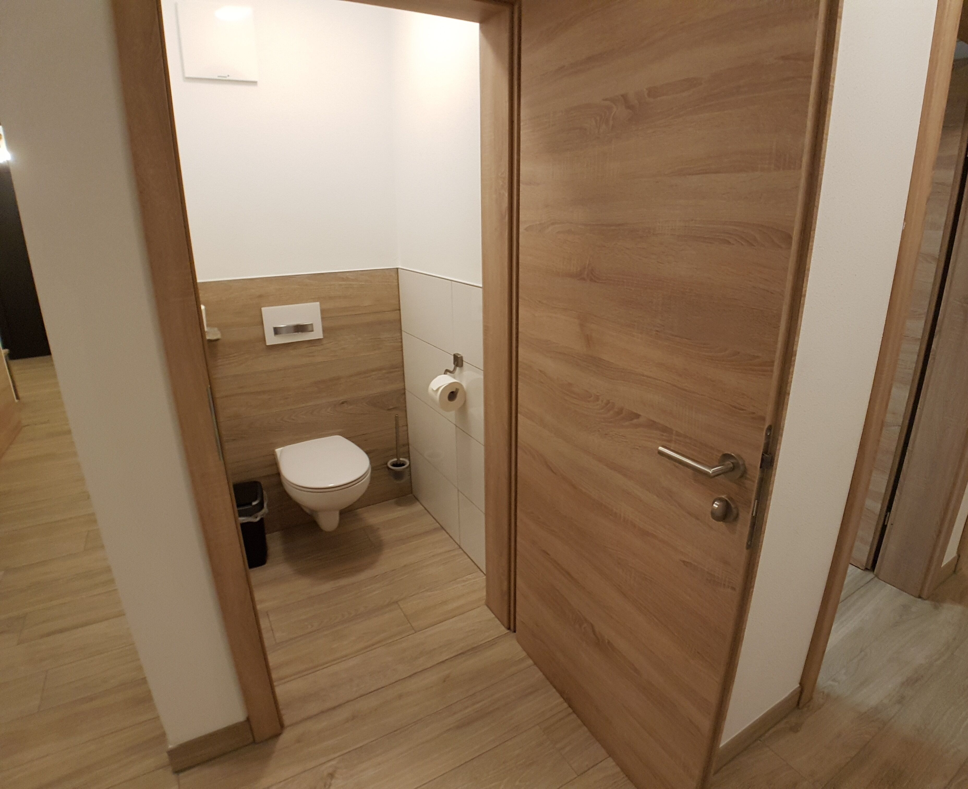 Een compacte, moderne badkamer met een houten vloer, een wit toilet en een houten deur.