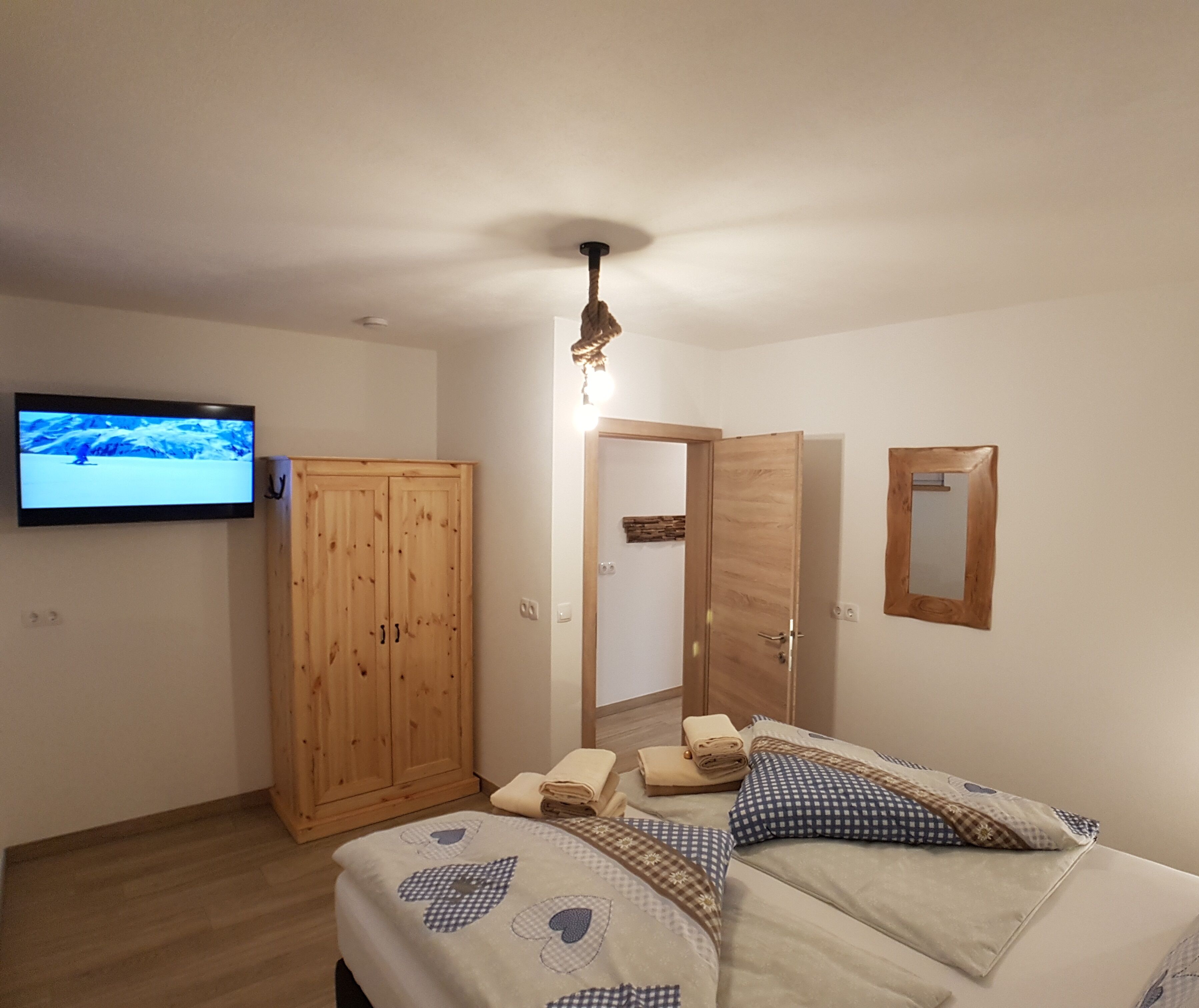 Quarto com cama, guarda-roupa de madeira, televisão e espelho.