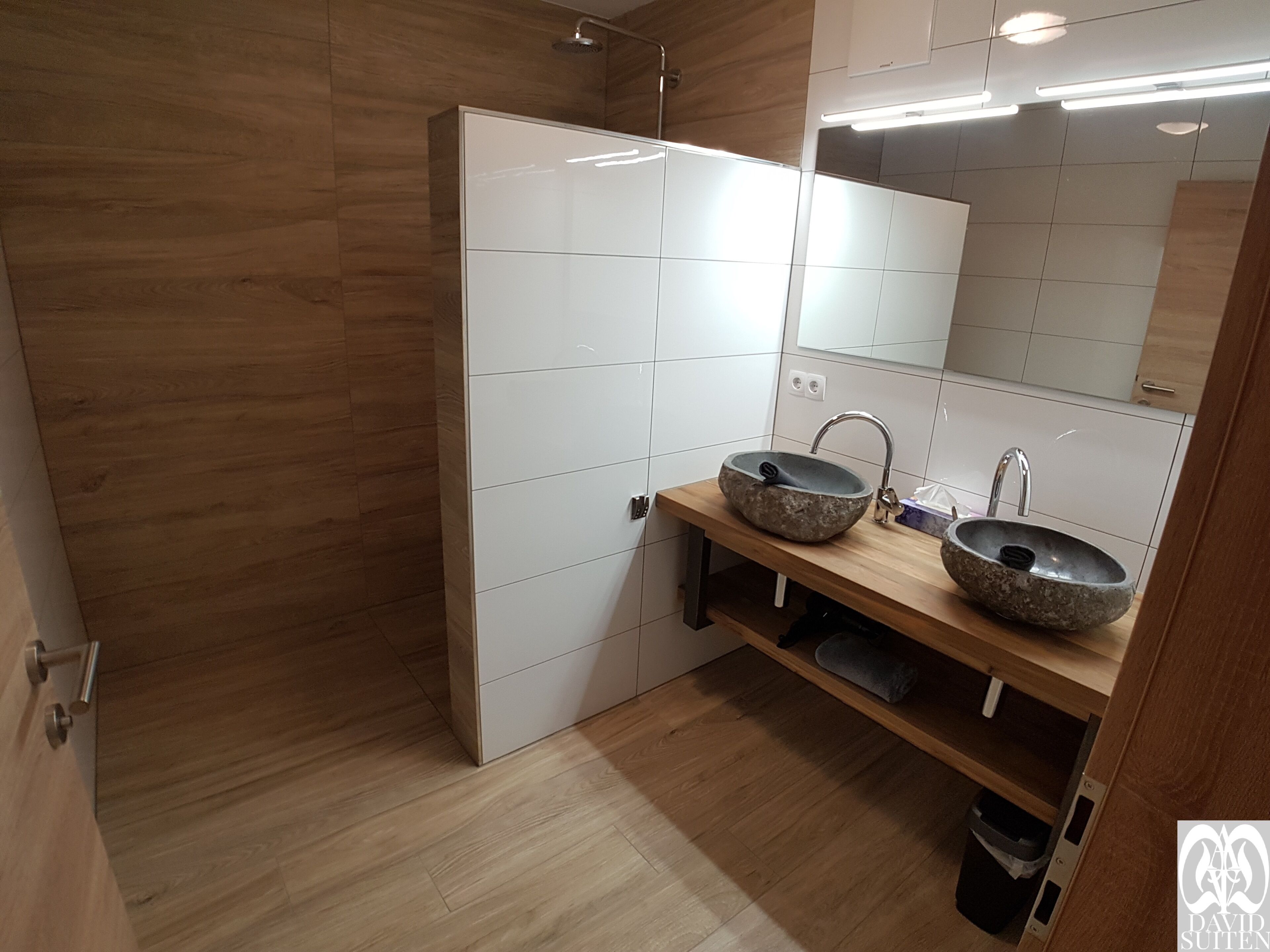 A modern bathroom with two stone sinks, wooden vanity, and a large mirror.
