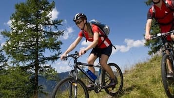 Two cyclists on a grassy hill with trees and mountains in the background.