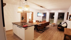 A modern kitchen with a central island, wooden dining table, and a cozy seating area with a sofa and armchair. - David Suiten (Mauterndorf)