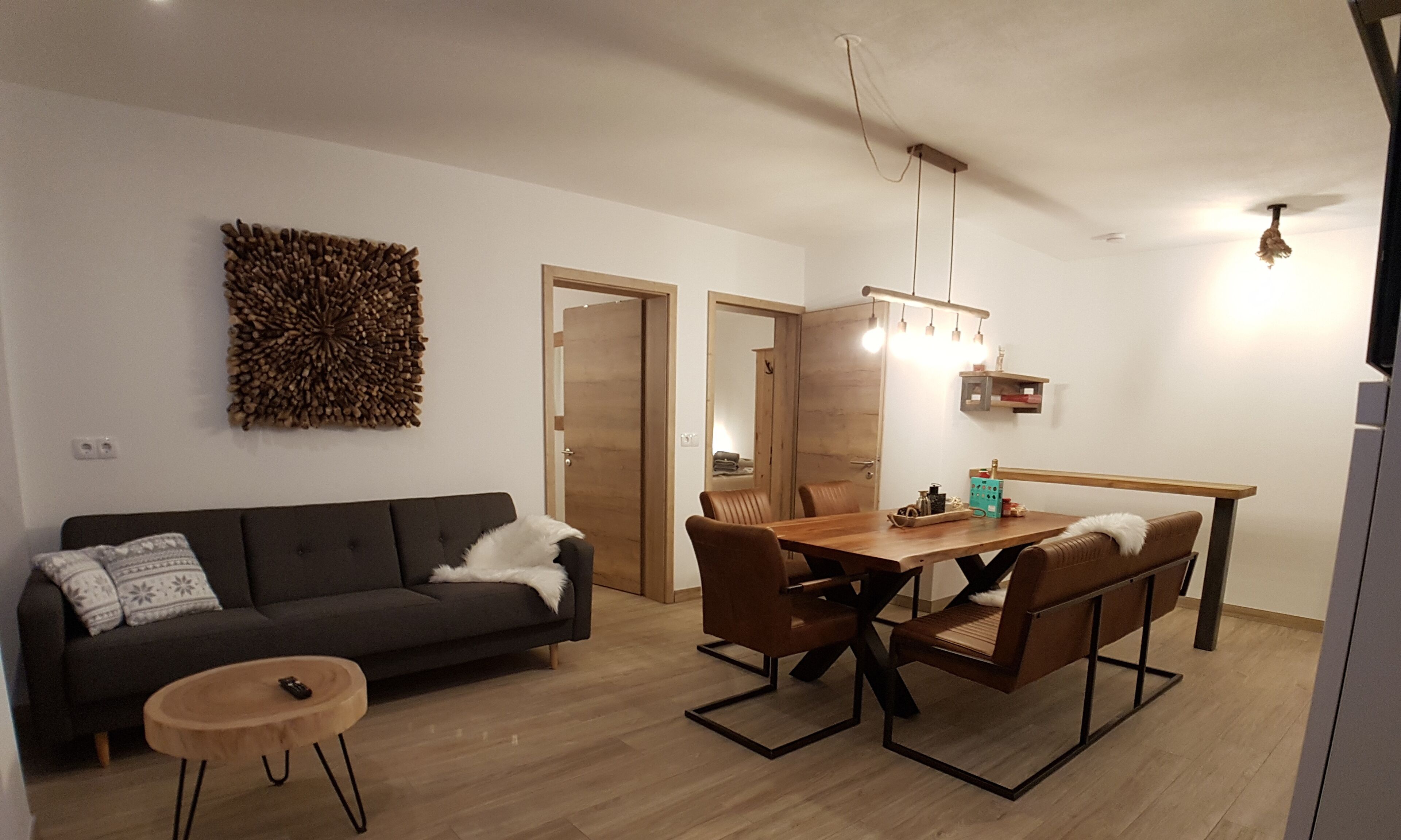 A modern living room with a dark grey sofa, a wooden coffee table, and a dining area with a wooden table and chairs.