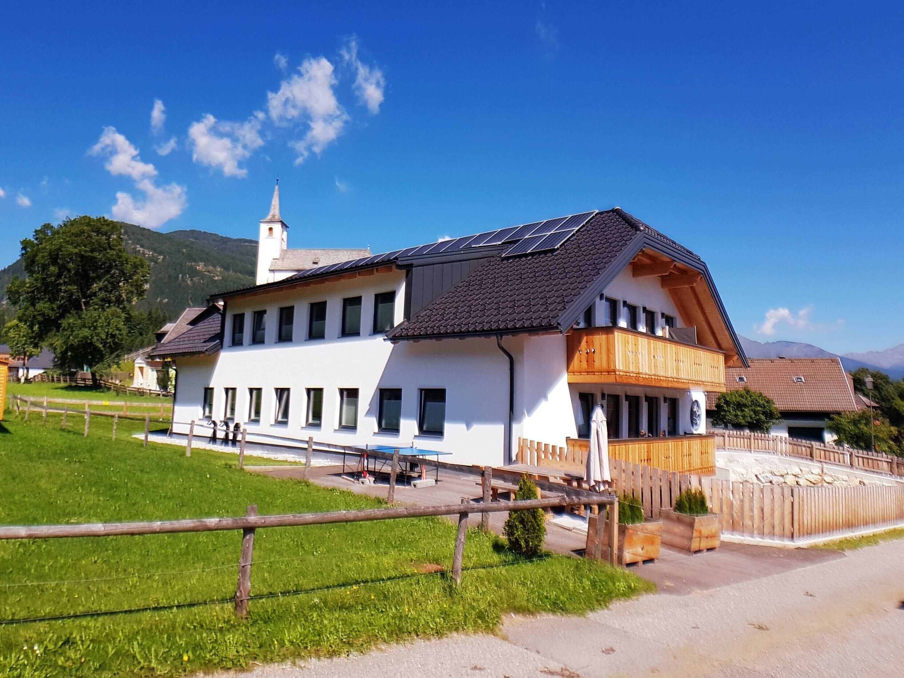 Un edificio de dos pisos con techo inclinado, paneles solares y un balcón.