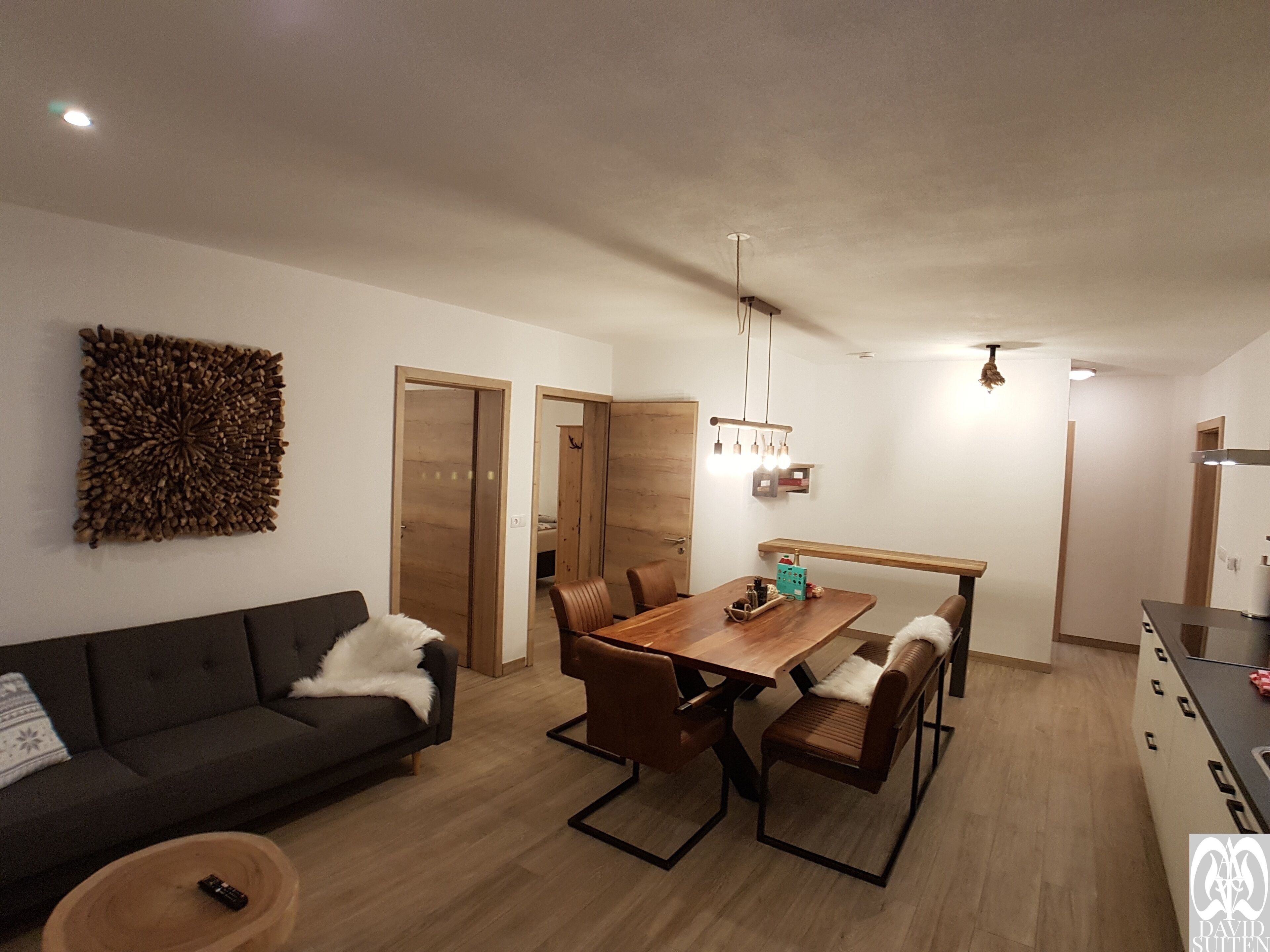 A modern living room with a dark sofa, a wooden dining table with chairs, and a decorative wall piece.
