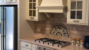 Et køkken med hvide skabe, et rustfrit stål køleskab, en gaskomfur og en dekorativ backsplash.
