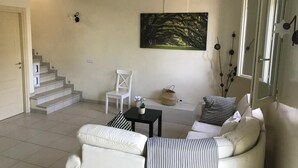 En stue med sofa, stol, lille bord og trappe op til et andet rum.