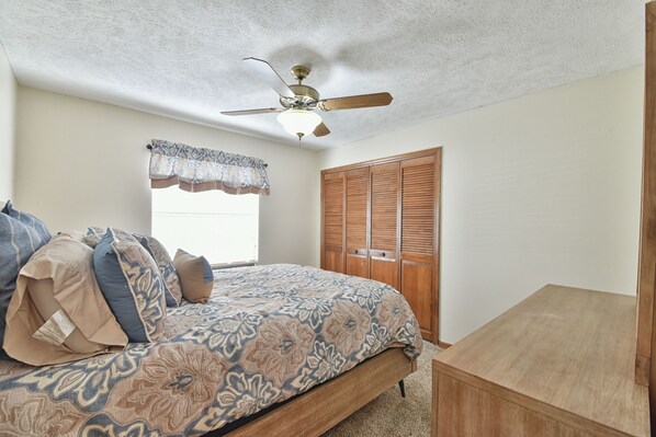 Un dormitorio con cama, ventilador de techo, ventana con cortina decorativa y puerta de madera.