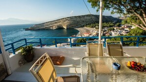 A balcony with a clear view of the sea, a chair, a table with fruit, and a potted plant. - Castri House in Matala (Matala)